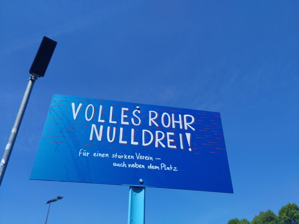 Ein Schild vor blauem Himmel, darauf steht "Volles Rohr Nulldrei!"