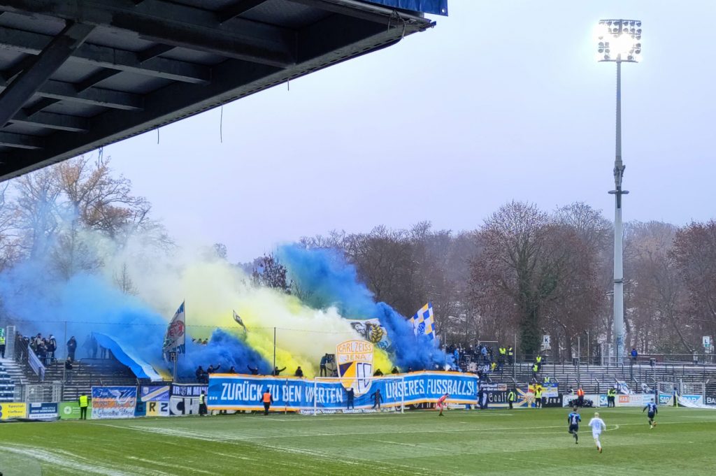 Fantribüne mit großen blauen und gelben Rauchschwaden und dem Banner "Zurück zu den Werten unseres Fußballs"
